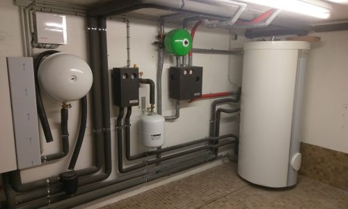 Technikraum mit Wärmespeicher, Ausdehnungsgefäßen und sauber verlegter Rohrinstallation an der Wand.